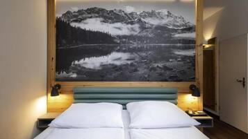 Un dormitorio con una cama, dos lámparas de noche y una gran fotografía enmarco de un paisaje montañoso.