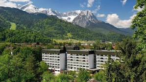 Un hôtel au design moderne, entouré d’une végétation luxuriante et de montagnes.