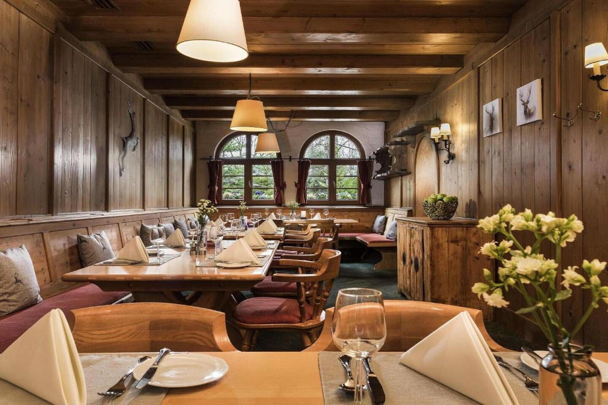 A wooden interior with tables and benches, arched windows, and wall-mounted light fixtures.