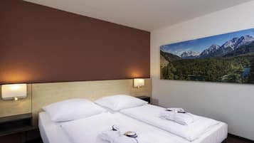 A hotel room with two beds, a headboard, wall-mounted lamps, and a large mountain landscape painting.