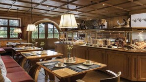 A rustic interior with wooden beams, a central island with kitchenware, and a seating area with tables and benches. - Sunday Hotel Garmisch Partenkirchen Junior Suite (Garmisch-Partenkirchen)
