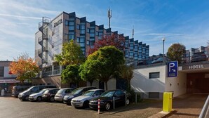 Ein Hotel mit modernem Design, ein Parkplatz mit mehreren Autos und ein sichtbares Schild, das einen Parkplatz kennzeichnet.