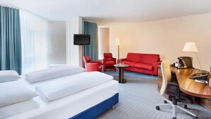 Ein Hotelzimmer mit einem Bett, einem Schreibtisch mit Stuhl, einem roten Sofa und einem Fernseher.