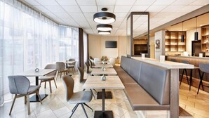 A modern hotel lobby with a long counter, seating area, and large windows.