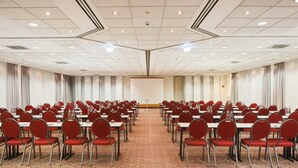 A conference room with rows of tables and chairs, a podium, and a large screen.