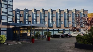 A modern hotel with a row of rectangular windows, a covered entrance, and a parking area.