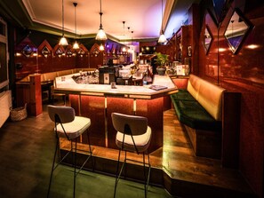Eine Bar mit Theke, zwei Barhocker, einer gepolsterten Bank und Pendelleuchten.