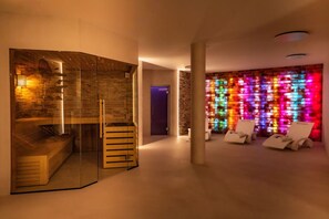 Ein modernes Interieur mit einer Glasabtrennung, einer Holzbank und einer farbenfrohen Wandleuchte. Im Vordergrund stehen zwei weiße Stühle.
