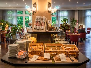Un bufé de desayuno con panes y bollería variados, revistas y una estación de café.
