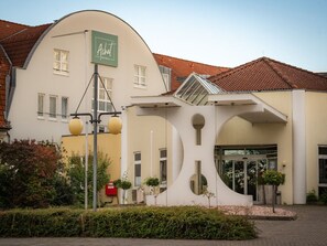 Ein modernes Gebäude mit einer geschwungenen Fassade, einem markanten Eingang mit Glastür und einem Schild für 'Achat Hotels'.
