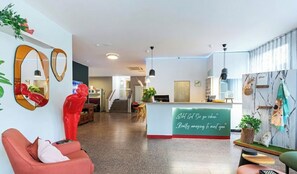 Un moderno vestíbulo de hotel con mostrador de recepción, zona de estar y una escalera que sube a otro piso.