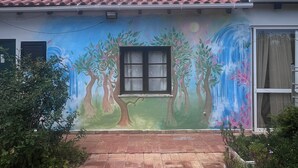 A building with a tiled roof, a mural of trees and flowers, a window, and a paved entrance. - Moinhos Velhos Juice Detox & Yoga (Lagos)