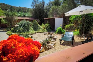 A garden with a variety of plants, a small shed, a bench, and a table with an umbrella. - Moinhos Velhos Juice Detox & Yoga (Lagos)