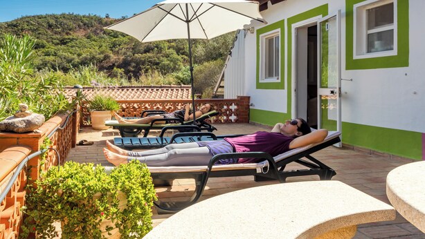 A sunlit outdoor relaxation area with lounge chairs and a large umbrella, overlooking a hillside. - Moinhos Velhos Juice Detox & Yoga (Lagos)
