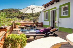 A sunlit outdoor relaxation area with lounge chairs and a large umbrella, overlooking a hillside. - Moinhos Velhos Juice Detox & Yoga (Lagos)