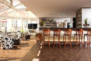 Eine moderne Bar mit Holzboden, einer hohen Decke mit Glasverkleidung und einer Theke mit Hockern.