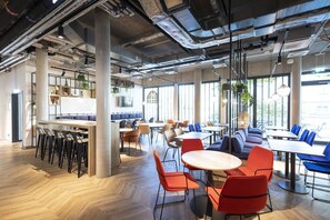 A modern dining area with high ceilings, exposed ductwork, and large windows allowing natural light. - Comfortable Superior Double Stay with Workspace | Pets are Allowed (Stuttgart)
