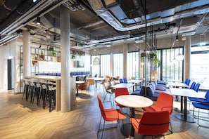 A modern dining area with high ceilings, exposed ductwork, and large windows allowing natural light. - Well-Appointed Superior Twin Room with Workspace (Stuttgart)