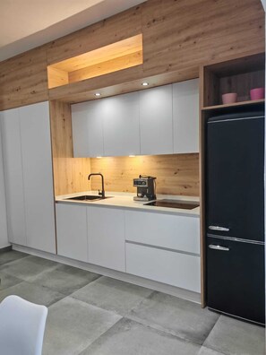 A modern kitchen with white cabinets, a black refrigerator, and a coffee machine. - Apartamento Fresno . (Chiclana)