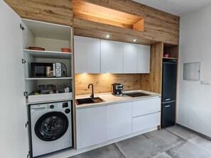 A compact kitchen with white cabinets, a built-in washing machine, a coffee maker, and a black refrigerator. - Apartamento Fresno . (Chiclana)