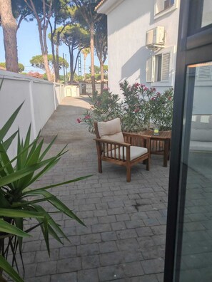 A patio area with a wooden chair and table, a potted plant, and a building with shutters. - Apartamento Fresno . (Chiclana)