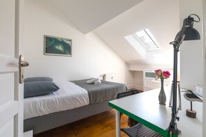 Quarto com cama, escrivaninha, cadeira, radiador, quadro na parede e claraboia.