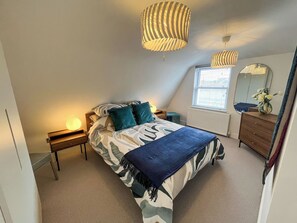 A bedroom with a bed, bedside lamps, a dresser, a mirror, and a window.