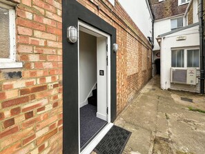 A narrow alleyway with a brick building, a door with a black frame, and a small step leading to a door.