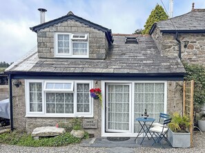 Ein Steinhäuschen mit Ziegeldach, einer Haustür und einer kleinen Terrasse mit Tisch und Stühlen.
