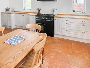 Una cocina con gabinetes blancos, una estufa negra y una mesa de madera con sillas.