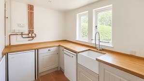 Una cocina con armarios blancos, encimera de madera, lavavajillas y una ventana con vistas a zonas verdes.