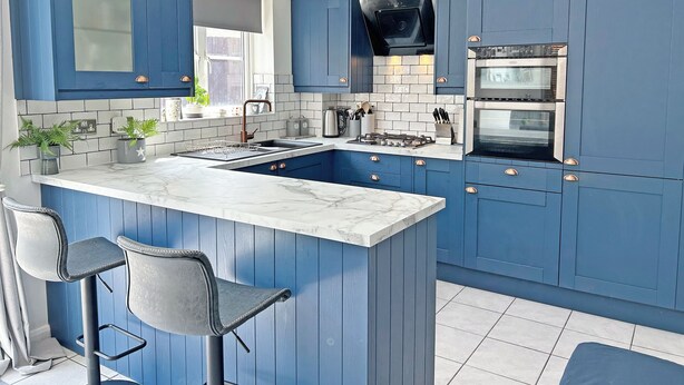 Una cocina con armarios azules, encimera de mármol y estufa a gas empotrada.