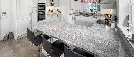 A modern kitchen with white cabinetry, a large granite island, and a built-in oven.
