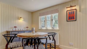 A dining area with a round wooden table, striped chairs, a window with a view, and a framed artwork on the wall.