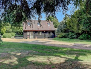A wooden cabin with a sloped roof, a front porch, and a gravel driveway. - 2 bedroom accommodation in Pulborough (Pulborough)