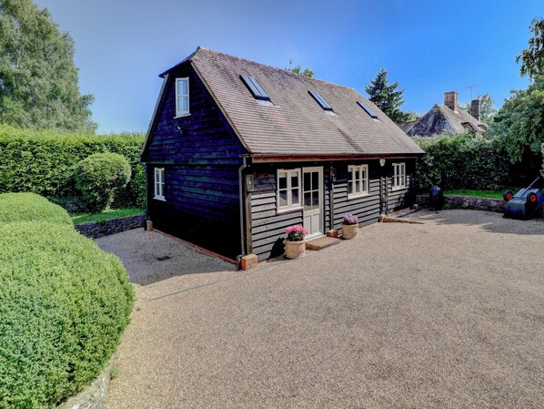 A small, dark wooden house with a sloped roof, a gravel driveway, and a well-maintained garden. - 2 bedroom accommodation in Pulborough (Pulborough)