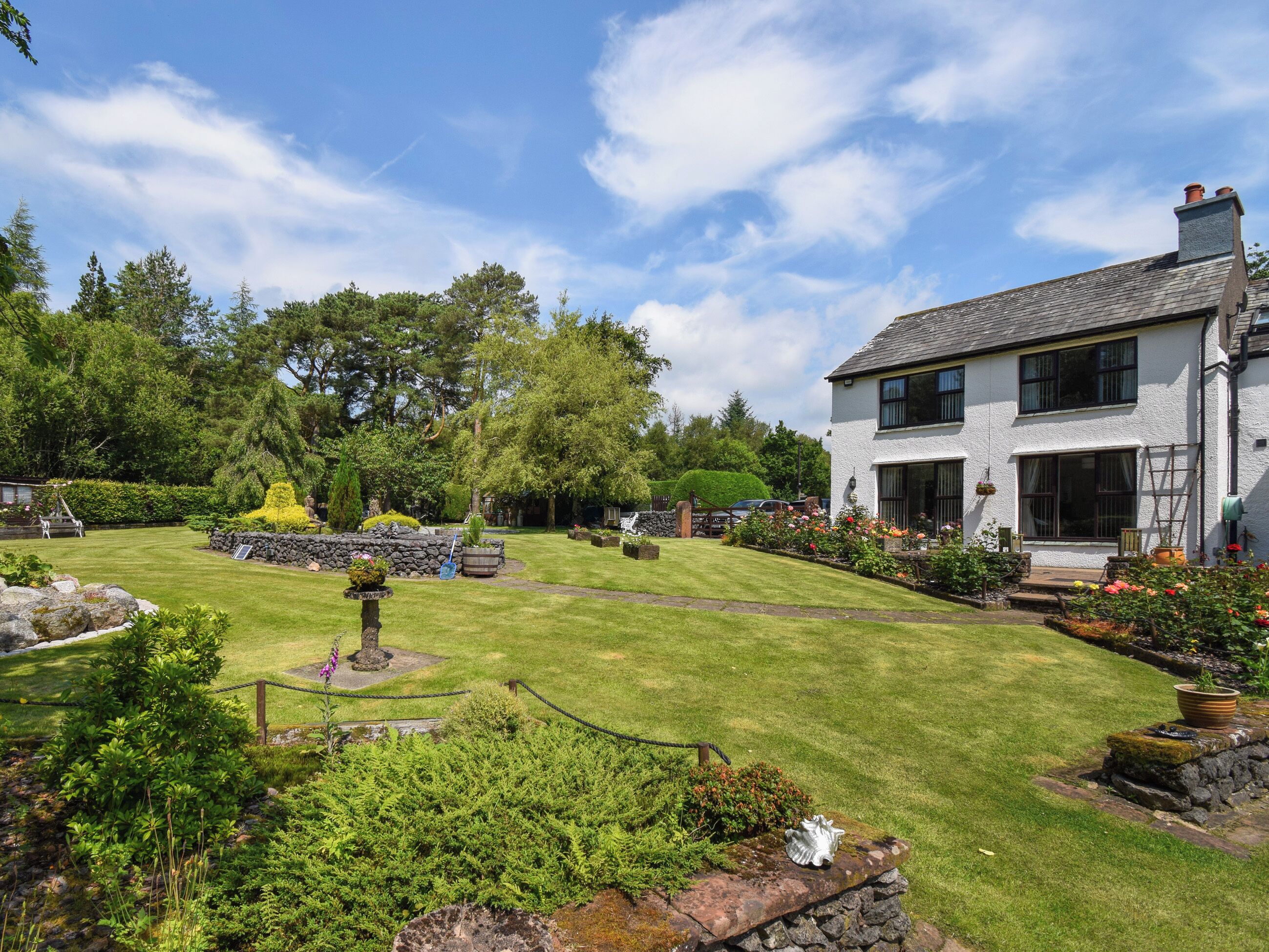 A well-maintained garden with a lawn, a stone wall, and a variety of plants and flowers.