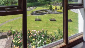 A view through a window of a well-maintained garden with a circular pond, neatly trimmed hedges, and flower beds. - 2 bedroom accommodation in Ennderdale (Ennderdale)