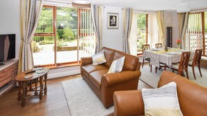 A living room with a brown leather sofa, a small wooden table, and a dining area with a table set for two. - 2 bedroom accommodation in Ennderdale (Ennderdale)