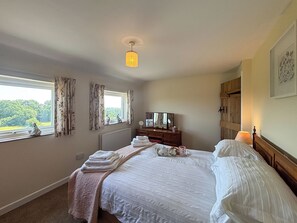 Ein Schlafzimmer mit einem Bett, einer Kommode, einem Fenster mit Vorhängen, einem Heizkörper und einer Wandlampe.