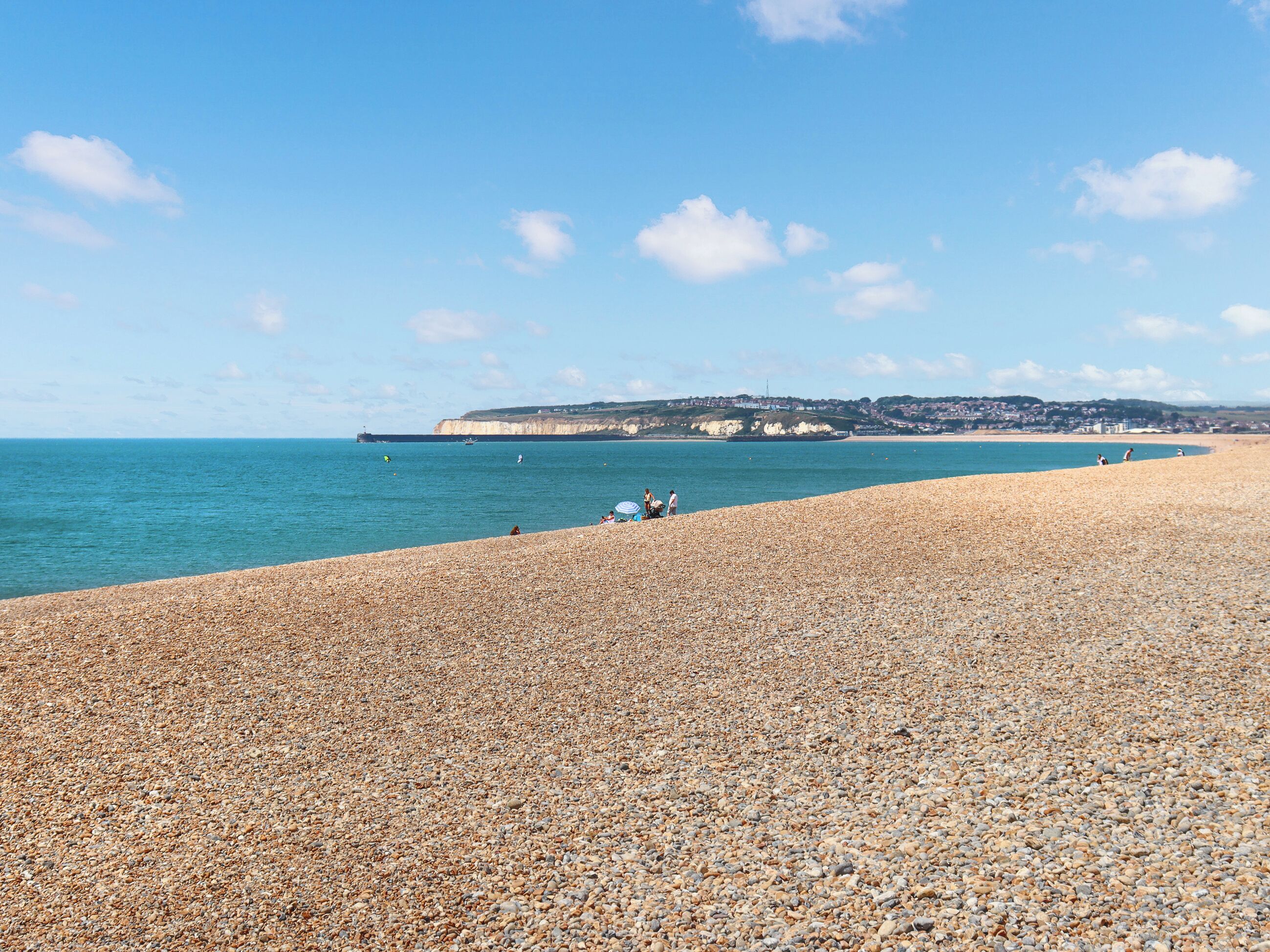 A pebbled beach with a clear view of the sea and distant cliffs.