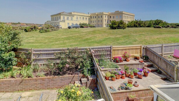 Un quartier résidentiel comprenant un grand immeuble, une pelouse verdoyante et une terrasse clôturée agrémentée de plantes en pot.