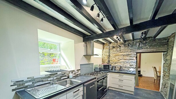 A modern kitchen with a stone accent wall, a window with a view, and a built-in dishwasher. - Hendre Aled Farmhouse (Llanssannan)