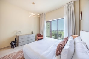 A hotel room with a large bed, a dresser, a chair, and a balcony with a view. - Bloomfields 2BR Fairways 2 Yas Golf  (Abu Dhabi)