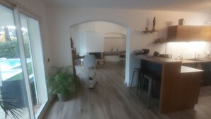 Un interior moderno con cocina, comedor y un amplio ventanal corredero que da a una piscina.