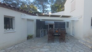 Un patio con suelo de piedra, una mesa, sillas y una parrilla de barbacoa integrada.