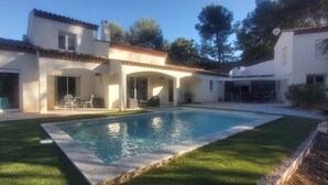 Una casa con piscina, un patio con sillas y una zona exterior cubierta.