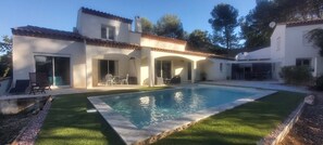 Ein Haus mit Swimmingpool, Terrasse mit Stühlen und überdachter Außenbereich.