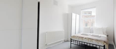A bedroom with a bed, a radiator, and a window with a view of buildings.