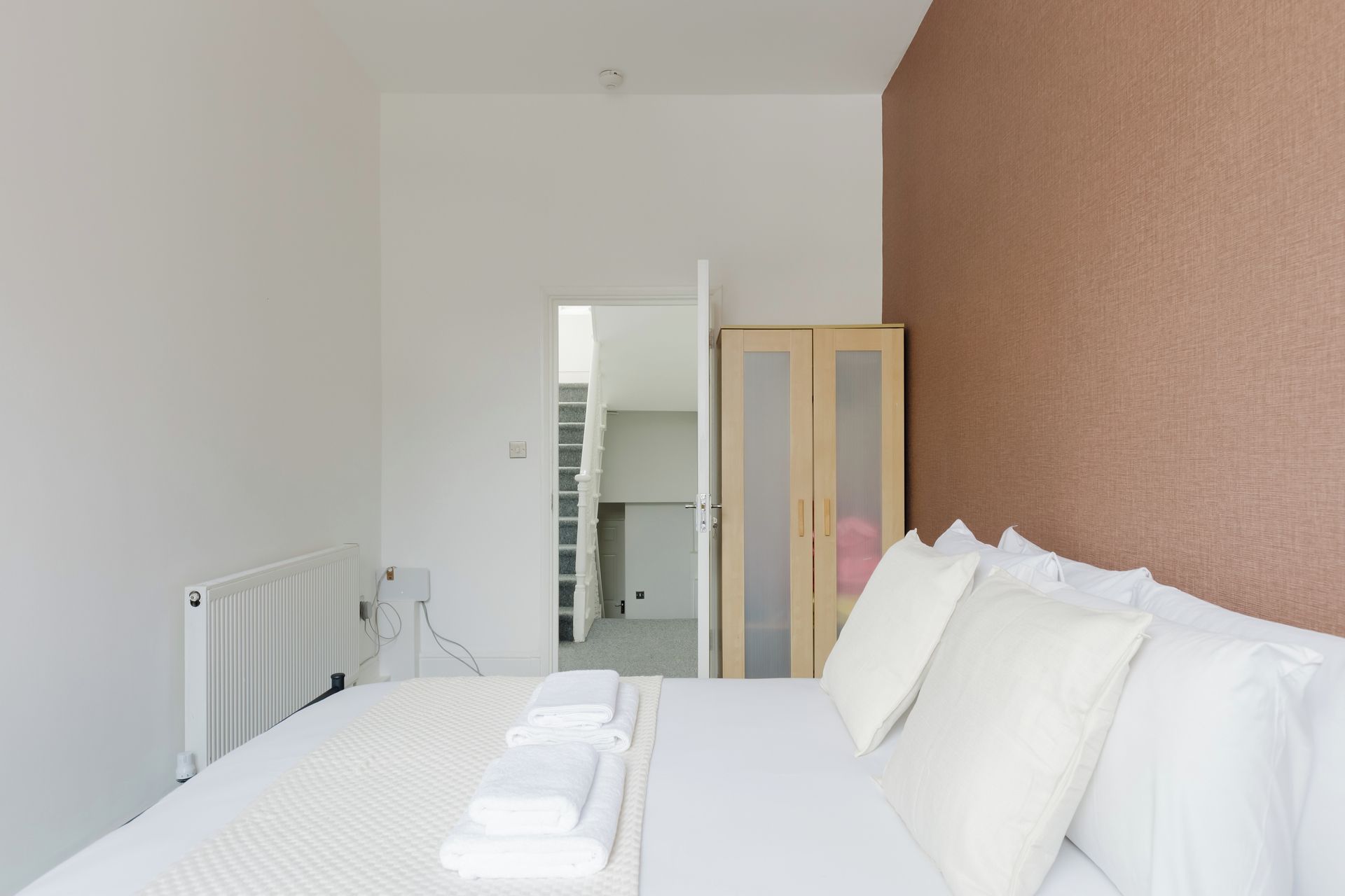 A hotel room with a bed, a wardrobe, and a view of a staircase.